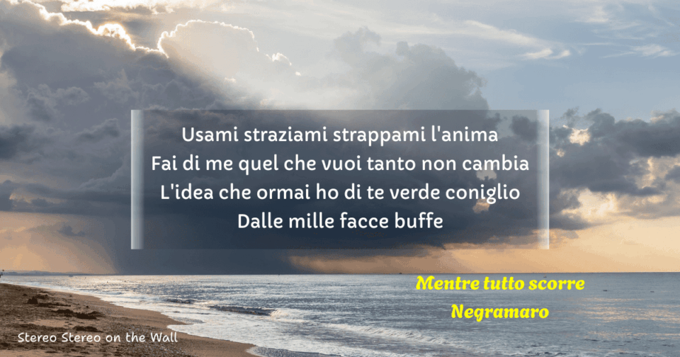 A panorama of a beach with dark clouds moving across the sky. The chorus of the song "Mentre tutto scorre" by the Italian band Negramaro is written above the image.